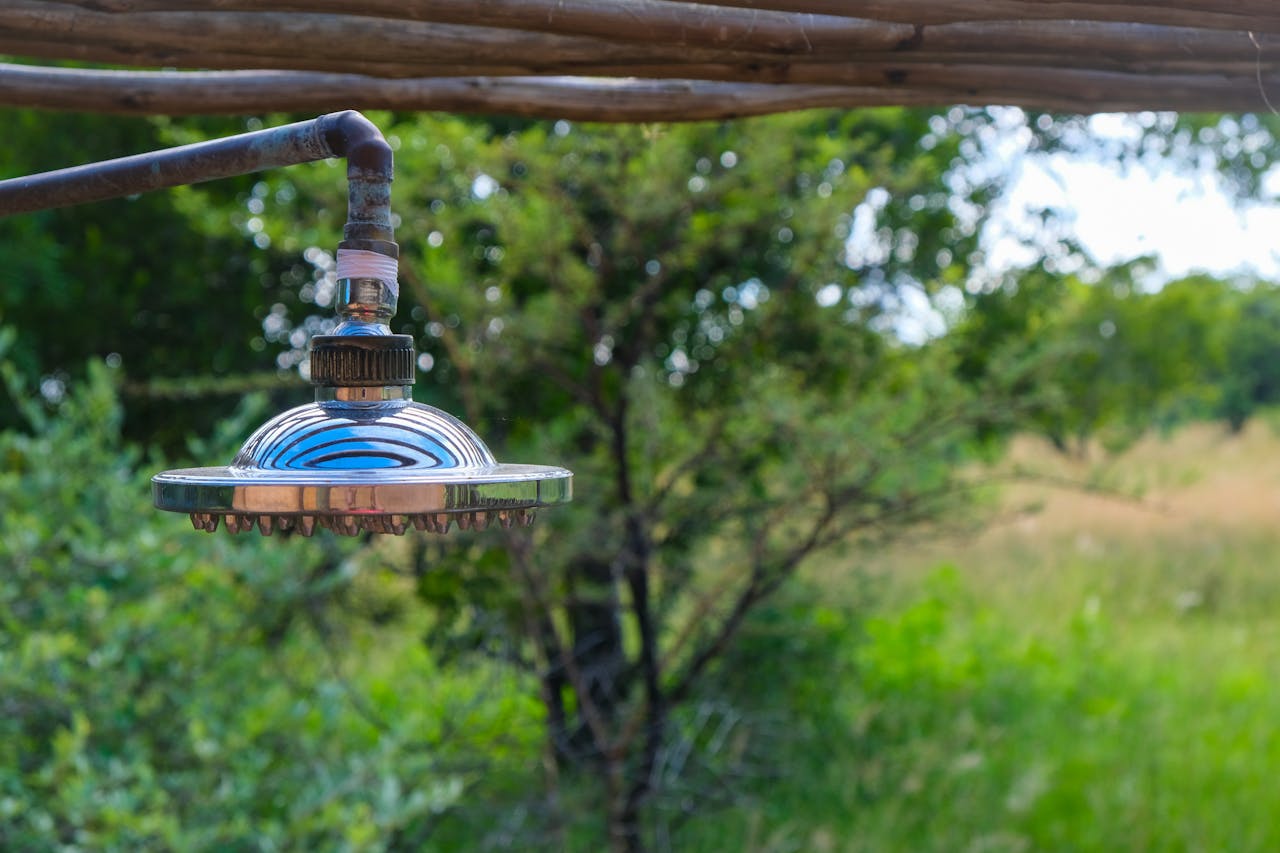 Close-up of a stainless steel shower head outdoors amidst lush green scenery.